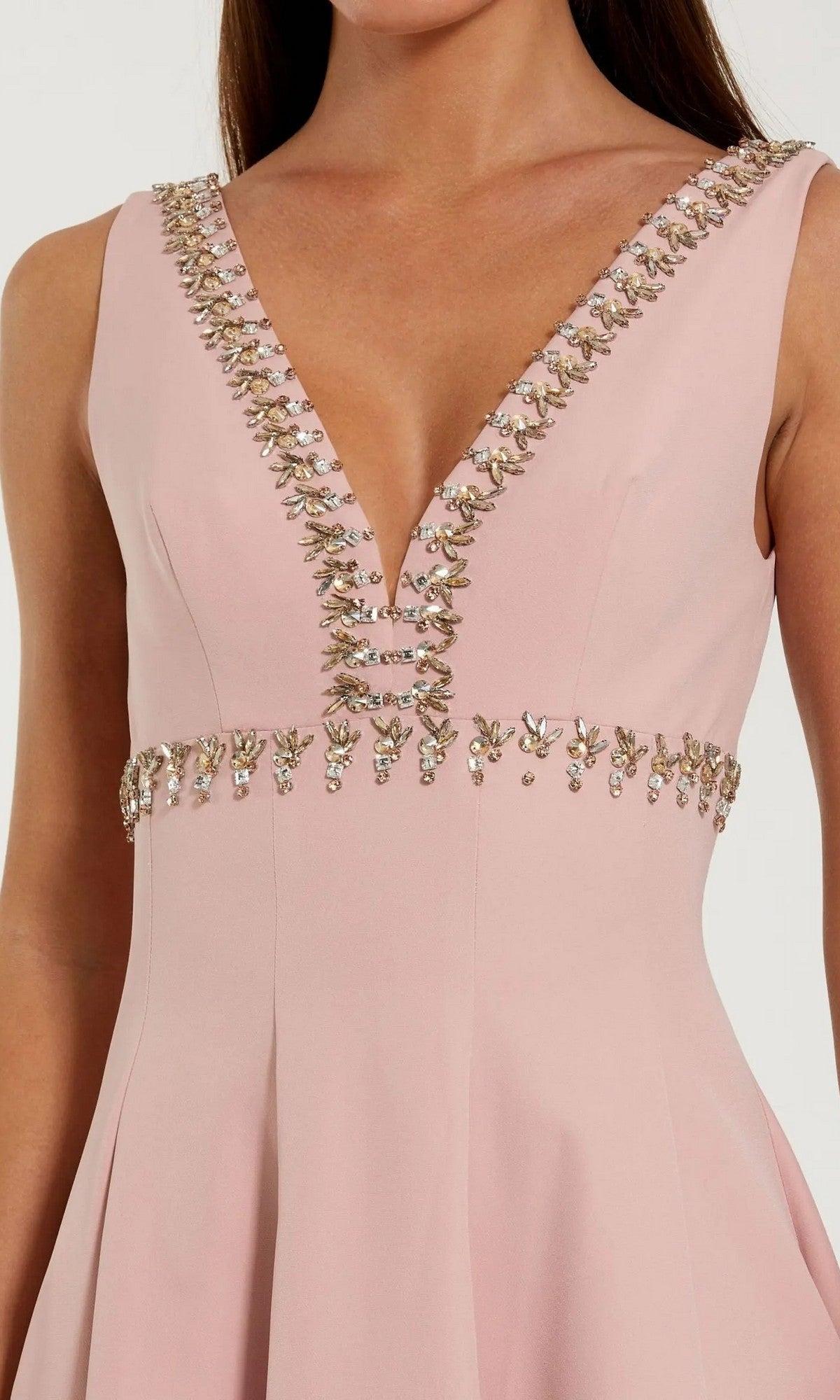 A woman wears the Midi Wedding Guest Dress: Mac Duggal 21159—a sleeveless light pink midi with a deep V-neckline and embellished details on the neckline and waist, making it a chic choice for any wedding guest.